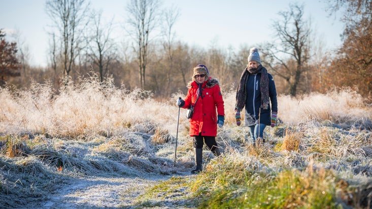 Two visitors walk through the parkland at Oxburgh Estate in Norfolk. Both are wearing their winter coats hats, scarves and gloves. There is a dusting of snow on the ground.